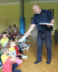 Policjant podaję książeczkę dziecku.