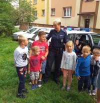 Policjantka i dzieci stoją przed radiowozem.